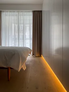 A minimalist bedroom featuring hardwood flooring and a fabric bed.