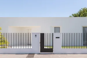 A modern house with a white exterior, concrete fence, and black metal gate.