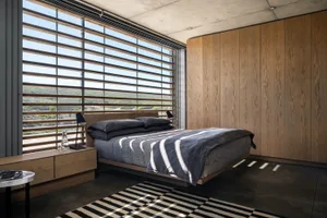 Minimalist bedroom featuring wooden furniture, concrete walls, and textiles