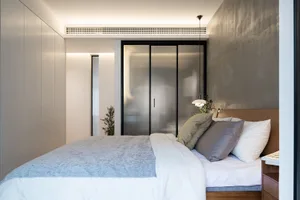 A minimalist bedroom featuring a bed with wooden frame, metal details, and a glass door wardrobe.