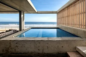 Modern minimalist outdoor space with a concrete pool, lounge area, and ocean view.