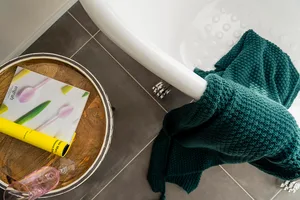A bathroom scene with a grey fiber blanket draped over a white bathtub and a book with a design on it placed on a wooden tray