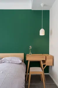 Modern minimalist bedroom featuring wooden furniture, green accent wall, and pendant light above the desk.