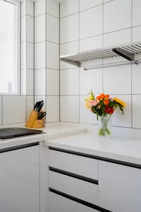 A minimalist kitchen with white ceramic tiles and black trim features a vase of colorful flowers on the countertop.