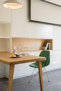 A modern minimalist kitchen featuring a wooden table and green chair, with a sleek white wall and built-in shelves.
