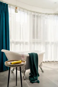 A modern bathroom interior featuring a ceramic bathtub, a decorative tray, and a hanging glass pendant light.