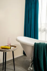A minimalist bathroom with a white bathtub, teal curtains, and black metal legs.