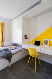 A minimalist bedroom with white furniture, yellow accents, and a built-in desk area.