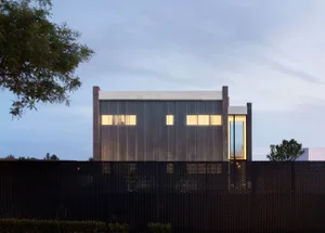 A modern architectural structure with a metallic wall, windows, and a black fence.