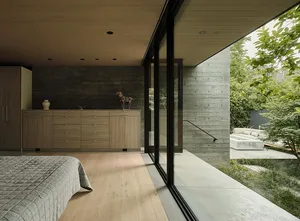 A modern bedroom featuring sliding glass doors and minimalist decor with concrete walls and wood flooring.