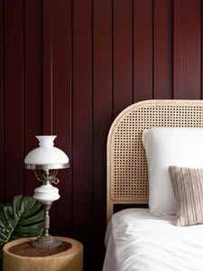 A modern bedroom featuring wood and cane furniture, white bedding, and a white table lamp with a white shade.