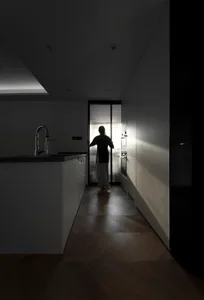 A modern black and white interior with a person standing in a kitchen setting, looking out a frosted glass window.