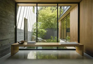 A modern interior space featuring wooden furniture, concrete walls, and large windows overlooking a garden.