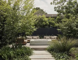 A modern outdoor space featuring concrete seating areas, wooden furniture, and lush greenery.