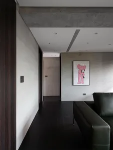 Contemporary living room featuring a black leather couch, a pink teddy bear painting, and a concrete finish on the walls and 