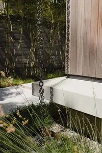 A black chain hanging down from a modern exterior wooden building with a concrete foundation and a concrete base platform.