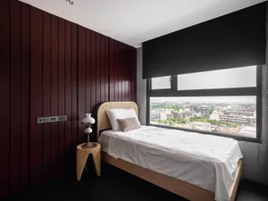 Minimalist bedroom with wood decor, featuring a single bed, nightstand, and large window overlooking a cityscape.