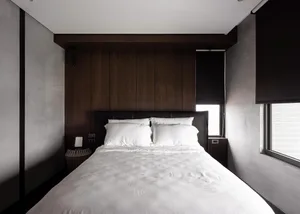 A modern minimalist bedroom with dark wood paneling and white bedding.