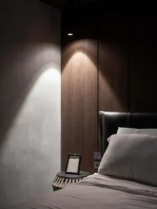 A modern minimalist bedroom featuring wooden paneling, a black headboard, and a small nightstand with a framed picture.
