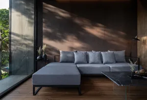 A modern living room featuring concrete walls, a spacious grey sofa, and a sleek black coffee table.