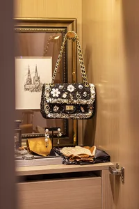 Luxurious black handbag adorned with floral embellishments and pearls, displayed on a wooden shelf with other fashion items i