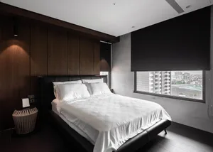 A modern minimalist bedroom with a black leather bed and white bedding, featuring dark wood walls and a large window with a c
