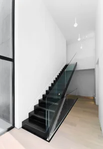 Staircase with black steps and glass railings in a minimalist interior setting.