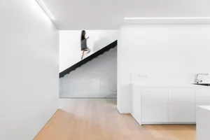 Modern residential apartment interior with white walls, wooden floor, black metal staircase, and white kitchen cabinets.