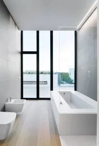 A modern bathroom with a minimalist design, featuring a concrete bathtub, a bidet, and a toilet with a light wooden floor.