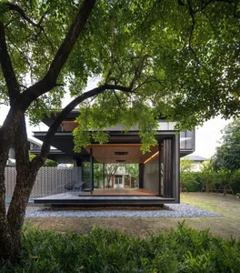 Modern house with glass walls and wooden deck surrounded by greenery.