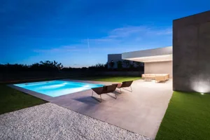 Modern outdoor pool deck made of concrete with lounge chairs and a sofa at dusk