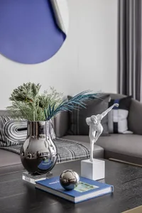 A modern interior design featuring a metallic vase with greenery, a porcelain statue of a dancer, an acrylic ball, and a book