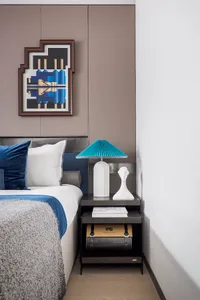 A modern bedroom featuring a double bed with blue bedding and white accents, accompanied by a black nightstand with a white l