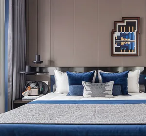 A modern bedroom featuring a bed with blue and white textiles, a nightstand with headphones, and a framed artwork on the wall