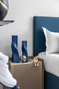 A modern bedroom with a blue upholstered headboard, white bedding, and a wooden nightstand with blue cylindrical decorations 