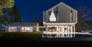 A modern residential building with a concrete exterior illuminated at night, featuring a lawn and a swimming pool.