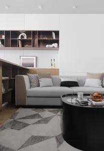 A modern, minimalistic Scandinavian living room with a gray and brown sofa, a round black coffee table, bookshelves, and a ge