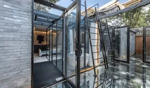 An industrial-style bathroom featuring clear glass walls, a white bathtub, and black accents.