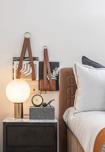 Modern bedroom with a brown upholstered bed, white and grey pillows, a nightstand with a spherical lamp, and decorative items
