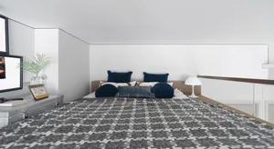A modern bedroom featuring a bed with a variety of colorful textiles, including a gray and white patterned bedspread and blue