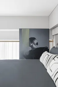 Modern minimalistic bedroom with gray bedspread and cushions, featuring a stylish wall art of a woman.