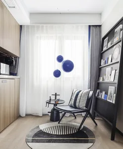A modern minimalist living room with dark furniture, white curtains, and blue spherical decorations.
