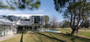 Modern residential home extension with a concrete facade, large glass windows, and a swimming pool in the garden.