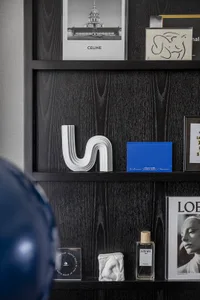 A modern black shelf with a combination of wood and concrete textures, displaying various decorative items including a Celine