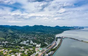 A landscape view of a city surrounded by hills and a river, featuring buildings and trees.
