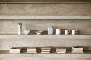 A display of ceramic white vessels including pitchers, bowls, and mugs arranged on a stone shelf.