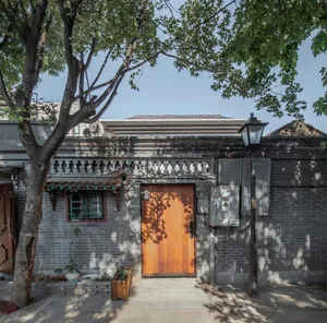A house exterior made of bricks with a wooden door and a tree casting shadows.