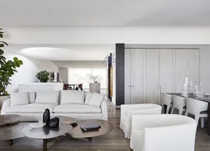 A minimalist living room featuring sleek, white furniture and wooden flooring.