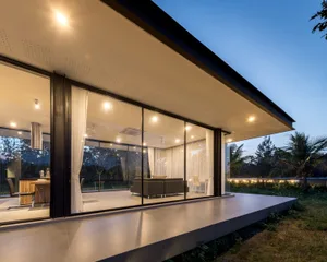 Modern residential exterior with large glass windows and concrete patio.