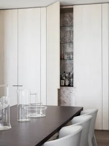 A modern kitchen with white storage cabinets, glassware, and bottles.
